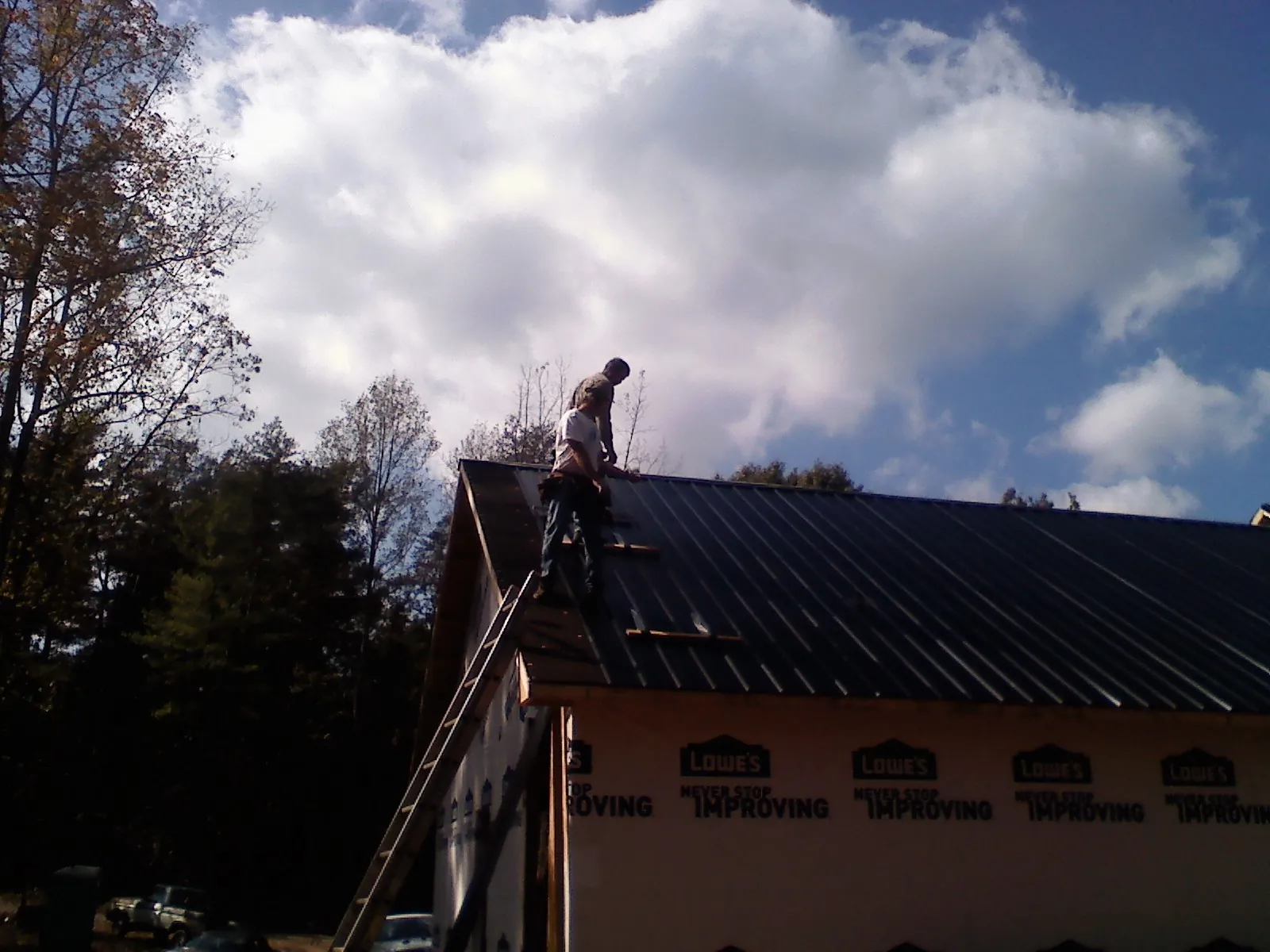 Roofer fastening dark metal panels high against a cloudy sky, from a Roof Inspection job in Bay City